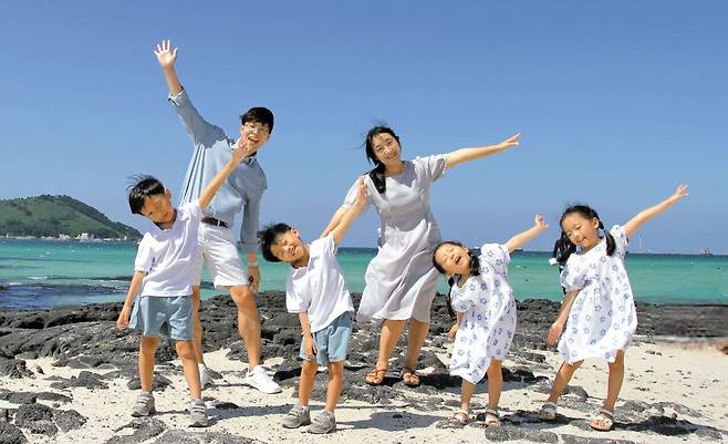 조정은(뒷줄 오른쪽)·이재혁 부부 가족이 지난해 9월 제주도에서 바다를 배경으로 팔을 활짝 벌리고 있다. 앞줄 왼쪽부터 첫째 지한(8), 여섯 살 삼둥이 수호, 지아, 수아. 이 사진은 서울시의 '엄마 아빠 행복한 순간 공모전'에서 참가상을 받았다. /조정은씨 제공