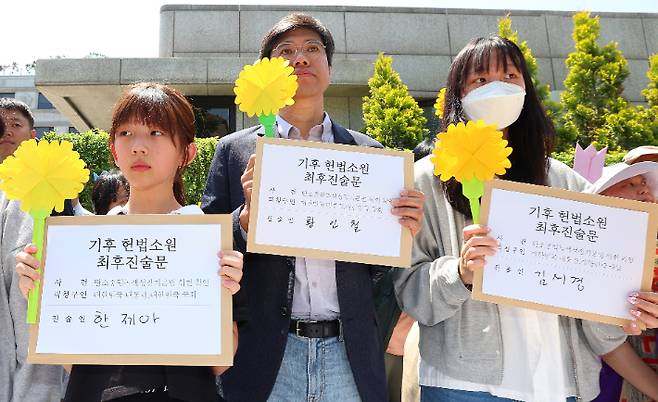 기후 헌법소원 마지막 공개변론일인 21일 서울 종로구 헌법재판소 앞에서 아기기후소송 청구인 한제아 어린이(왼쪽부터), 시민기후소송 청구인 황인철·청소년기후소송 청구인 김서경 씨가 기자회견을 마친 뒤 최후진술문을 들고 사진 촬영을 하고 있다. 연합뉴스