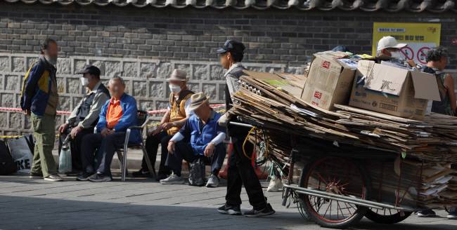 팍팍한 노년의 삶… 12일 오전 서울 종로구 원각사에서 무료 급식을 받으려 줄을 선 노인들 옆으로 한 폐지 줍는 노인이 리어카를 끌며 지나가고 있다.  윤성호 기자