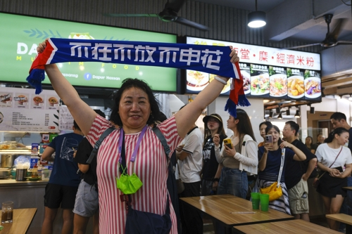 한 중국 축구팬이 14일 싱가포르 축구 국가대표팀 골키퍼 하산 서니가 운영하는 노점 식당 앞에서 포즈를 취한 모습. [사진 출처 = 연합뉴스]