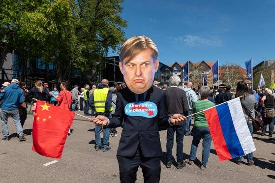 지난 4월  ‘독일을 위한 대안(AfD)’ 소속 극우 정치인 막시밀리안 크라의 마스크를 쓴 시위자가 중국과 러시아 국기를 들고 가슴에 ‘독재자를 위한 대안’이라는 팻말을 붙이고 서 있다. 막시밀리안 크라는 보좌관이 중국 스파이 혐의로 체포됐고, 스스로도 중국과 러시아로부터 의심스러운 금품을 받은 혐의로 조사를 받았다. [AFP=연합뉴스]