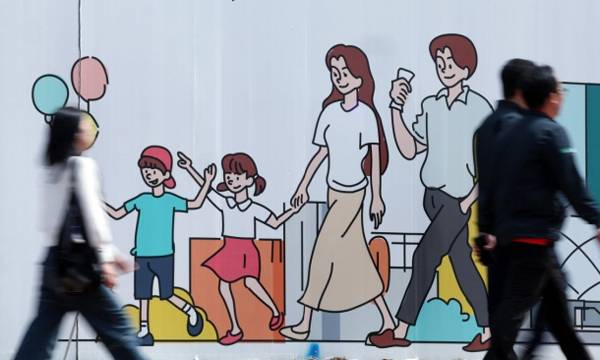 서울 도심의 공사장 가림막에 그려진 행복한 가족 그림 앞으로 시민들이 지나고 있다.&nbsp;뉴스1