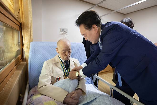 윤석열 대통령이 21일 경기도 수원시 장안구 보훈요양원을 방문해 '영웅의 제복' 재킷을 입은 6·25 참전 국가유공자의 옷매무새를 고쳐주고 있다. [연합]