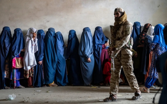 아프가니스탄에서 부르카를 뒤집어쓴 여성들을 배경으로 탈레반의 한 남성 경비병이 소총을 들고 걷고 있다. / 사진=AP 연합뉴스 자료사진