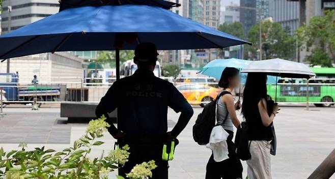 서울 한낮 기온이 30도까지 오른 지난 11일 오후 서울 종로구 광화문 광장에서 그늘막 아래 근무하는 경찰 앞으로 양산을 쓴 시민들이 지나기고 있다. 연합뉴스