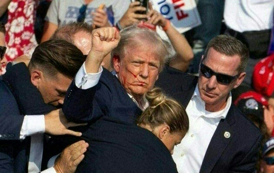 Former U.S. President Donald Trump, center, pumps his fist at the crowd after a shooting at a campaign rally in Butler, Pennsylvania, Saturday. The Republican candidate is seen with blood on his face surrounded by Secret Service agents as he is taken off the stage. [AFP/YONHAP]