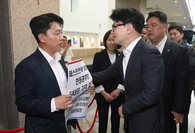 한동훈 국민의힘 당대표 후보가 18일 서울시의회에서 열린 국민의힘 서울시의원 간담회에 참석하기 전 ‘패스트트랙 투쟁 폄훼 한동훈 후보 당대표 자격 없다’라고 적힌 손팻말을 든 이희원 서울시의원과 대화하고 있다. 공동취재사진