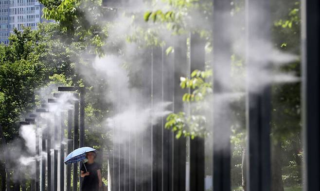 지난 25일 오후 부산 부산진구 부산시민공원에서 양산을 쓴 시민이 쿨링포그를 맞으며 이동하고 있다. 뉴스1