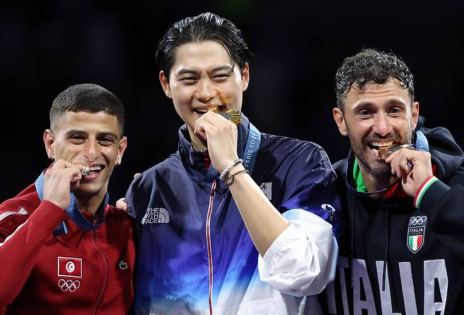 대한민국 펜싱 대표팀 오상욱 선수가 27일(현지시각) 프랑스 파리 그랑 팔레에서 열린 2024 파리올림픽 남자 사브르 개인 결승 시상식에서 금메달을 깨물어보이고 있다. 왼쪽은 은메달을 수상한 튀니지의 파레스 페르자니 선수, 오른쪽은 동메달을 수상한 이탈리아의 루이지 지멜리. /뉴스1