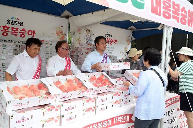 신영재 홍천군수(사진 가운데)가 1일 서울양양고속도로 휴게소 로컬푸드 행복장터에서 12브릭스 이상의 고품질 홍천 대홍복숭아를 홍보하고 있다. 홍천군 제공