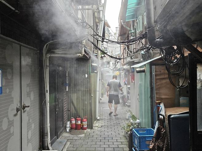 폭염주의보가 내려진 지난 29일 오후 1시께 종로3가 돈의동 쪽방촌. 2분 주기로 수증기를 뿜어내는 쿨링포그 아래로 주민이 더위를 식히며 걸어가고 있다. [사진=지혜진 기자]