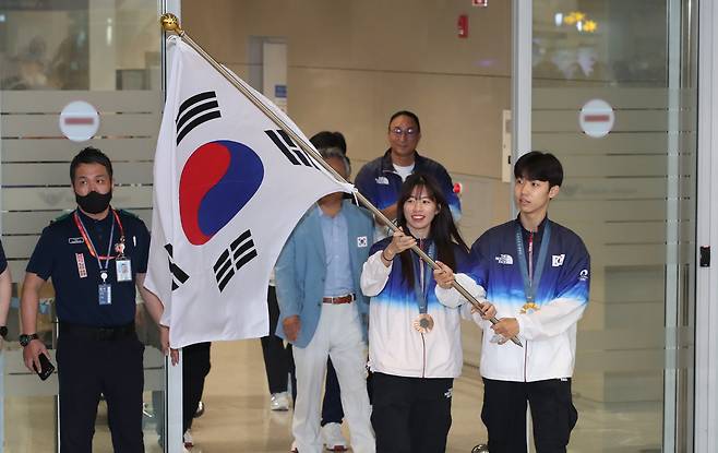 Boxer Im Ae-ji, left, and Taekwondo practitioner Park Tae-joon, right, arrive at Incheon International Airport on Tuesday holding the Korean national flag. Park won a gold medal in the men’s -58-kilogram category to bring home the country’s first gold in taekwondo since 2016, while Im secured bronze in the women's bantamweight category to become the first female Korean boxer to medal at the Games. [NEWS1]