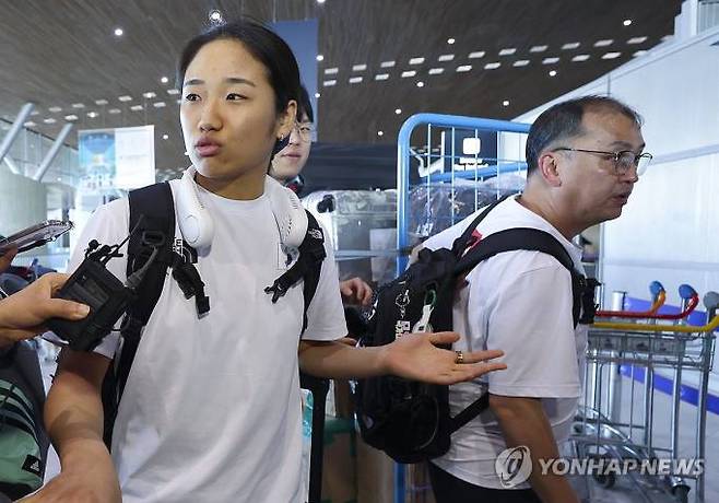 여자 배드민턴 단식에서 우승해 금메달을 획득한 안세영이 6일 오후(현지시간) 프랑스 파리 샤를 드골 공항을 통해 귀국하기 위해 도착한 뒤 취재진 질문을 받고 있다. 안세영 옆으로 김학균 배드민턴팀 감독이 지나가고 있다. [연합뉴스]