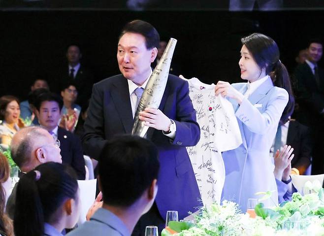윤석열 대통령과 부인 김건희 여사가 22일 서울 한 호텔에서 열린 2024 파리올림픽 선수단 격려 행사에서 마술사 이은결의 공연 중 탁구 전지희로부터 선물받은 선수단 사인 성화봉과 티셔츠를 보여주고 있다. ⓒ뉴시스