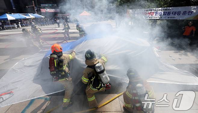 지난 28일 서울 성동구 왕십리광장에서 열린 성동구, 성동소방서와 전기차 화재 대응 합동 훈련에서 소방관들이 불이난 전기차에 질식소화 덮개로 화재를 진압하고 있다. 이날 훈련은 주차 중이던 전기차에 원인을 알 수 없는 불이 난 상황을 가정해 진행됐다. 2024.8.28/뉴스1 ⓒ News1 박지혜 기자