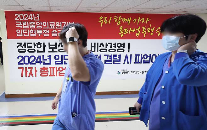 Medical workers pass by a poster posted at the National Medical Center that informs about unionized hospital workers' strike. (Yonhap)