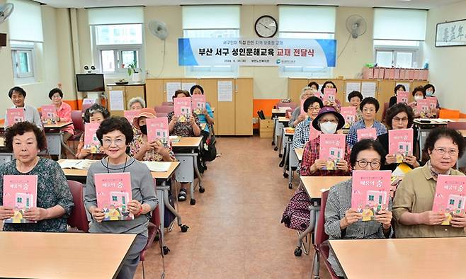 지난달 30일 부산 서구 평생학습관 수강 어르신들이 문해교육 교재 ‘배움의 숲’을 들어보이며 활짝 웃고 있다. 부산 서구 제공