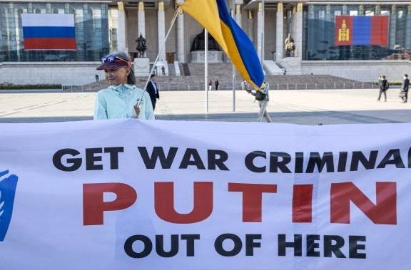 블라디미르 푸틴 러시아 대통령이 몽골을 방문한 2일(현지시간) 수도 울란바토르 시내에서 한 여성이 우크라이나 국기를 든 채 ‘전범 푸틴은 즉각 여기서 나가라’라고 적힌 현수막을 펼치며 시위를 하고 있다. AFP연합뉴스