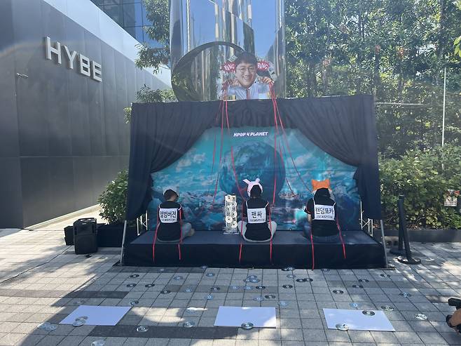 Kpop4Planet climate activists throw CDs behind them to the ground to protest K-pop agencies' marketing tactics that encourage fans to make excessive album purchases, in front of Hybe's headquarters in Yongsan-gu, Seoul, Wednesday. (Kim Jae-heun/Korea Herald)