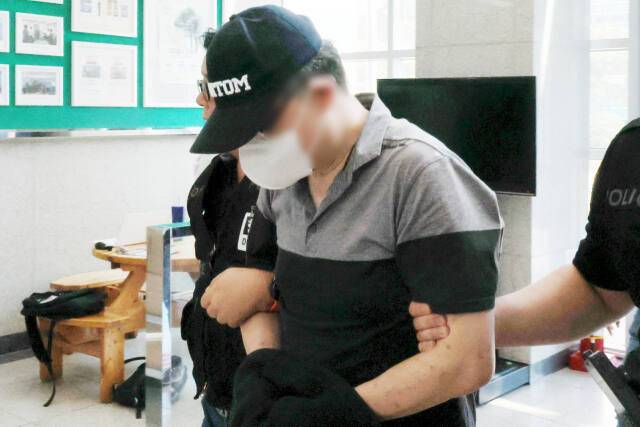 직장 동료 살해 혐의를 받고 있는 50대 남성이 수갑을 찬 채 경찰서 내부로 들어오고 있다. [사진 연합뉴스]
