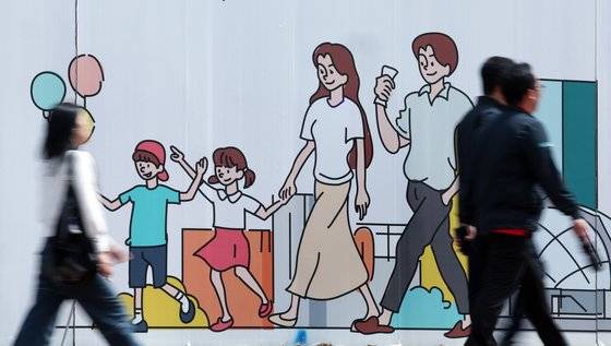 서울 도심의 공사장 가림막에 그려진 행복한 가족 그림 앞으로 시민이 지나고 있다. 지난 1일 한반도미래연구원은 전국의 20~49세 남녀 2천명을 대상으로 결혼과 출산에 대한 심층 인식조사를 벌인 결과, 20~49세 남녀 43% 가까이는 출산할 의향이 없는 것으로 나타났다고 밝혔다.