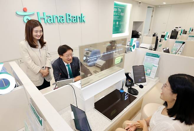 Hana Bank CEO Lee Seung-lyul, second from left, seats behind a bank teller window on which a real-time translation is displayed at the bank's Pyeongtaek Foreign Customer Center in Gyeonggi on Thursday. [HANA BANK]