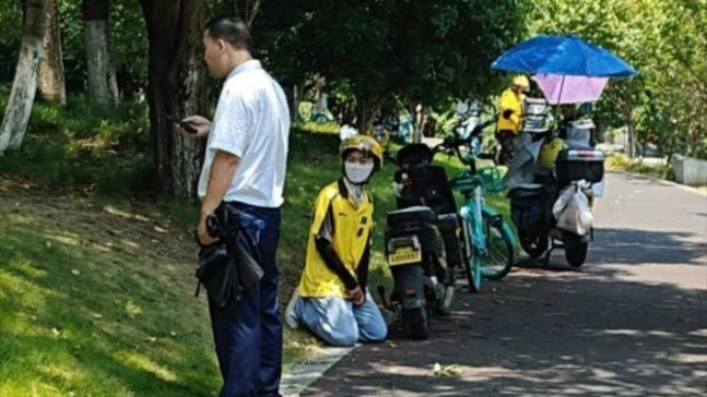 지난달 12일 중국 항저우의 한 아파트 앞에서 배달원(노란색 자쳇)이 무릎을 꿇고 사죄하고 있다. 화단을 망쳤다는 이유로 경비원 앞에서 용서를 구하던 것으로 알려졌다. [이미지출처=바이두 캡처]