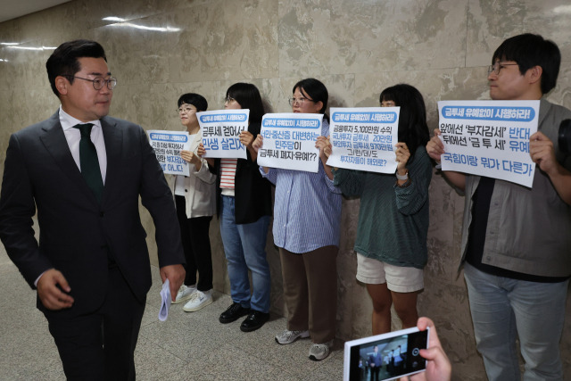 ▲지난 24일 오전 금융투자소득세 시행에 대한 더불어민주당의 '정책 디베이트'가 열린 민주당 의원총회장 앞에서 경제정의실천시민연합(경실련)과 참여연대 회원들이 금투세 시행을 촉구하고 있는 앞을 박찬대 민주당 원내대표가 지나가고 있다. ⓒ연합뉴스