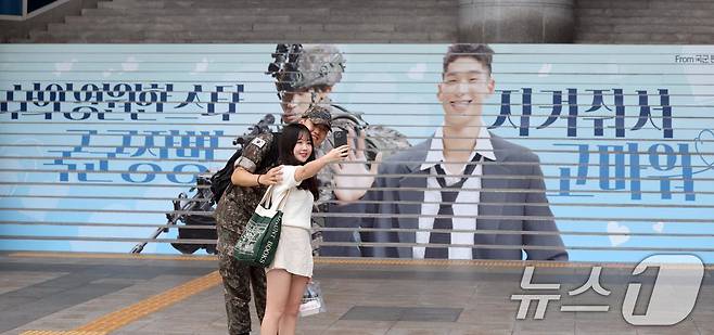 군 장병과 시민이 서울 용산역 광장에 게시된 광고를 배경으로 사진을 찍고 있다. (국방부 제공) 2024.9.20/뉴스1