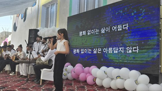 준공식을 한 학교 주위에도 지진으로 집을 잃은 사람들이 사는 텐트가 보였다(위). 학교 준공식에서 한 학생이 평화의 소중함을 담은 노래를 부르고 있다. 뒤로 노래의 가사가 보인다. 백성호 기자