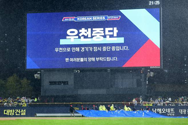 21일 광주 기아챔피언스필드에서 열린 2024 신한 SOL뱅크 KBO 포스트시즌 한국시리즈 1차전 삼성 라이온즈와 기아(KIA) 타이거즈의 경기. 6회초 강한 비로 경기가 잠시 중단되자 경기장 관계자들이 방수포를 경기장에 덮고 있다. 연합뉴스