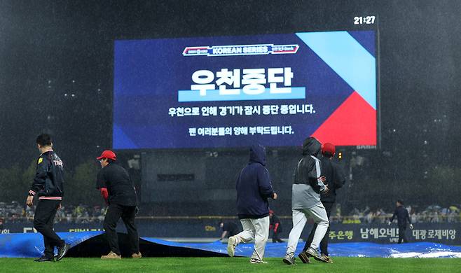 21일 광주 기아챔피언스필드에서 열린 2024 신한 SOL뱅크 KBO 포스트시즌 한국시리즈 1차전 삼성 라이온즈와 KIA 타이거즈의 경기. 6회초 강한 비로 경기가 잠시 중단되자 경기장 관계자들이 방수포를 경기장에 덮고 있다. 연합뉴스