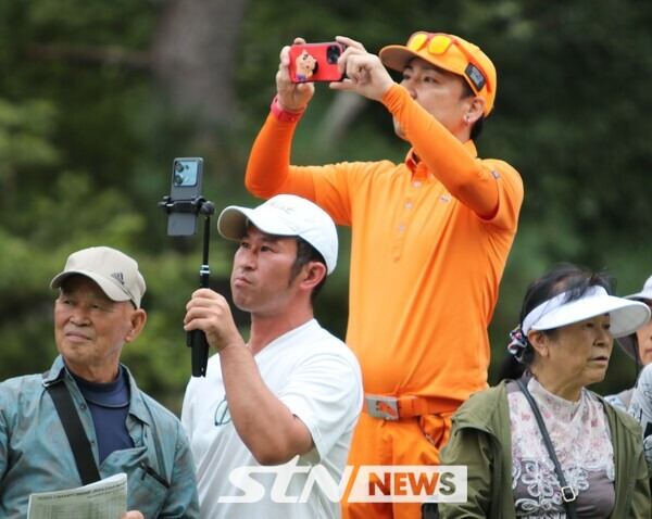 '오렌지 보이'로 유명한 리키 파울러의 시그니처 의상을  입고 일본 팬이 파울러의 티샷 영상을 찍고 있다. 사진┃STN NEWS