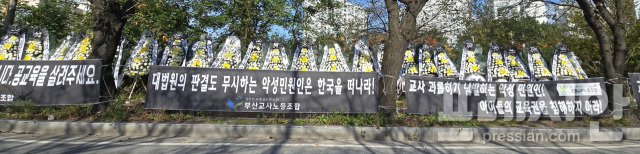 ▲A초등학교에 악성민원을 제기하는 학부모가 근무하는 직장 진입로 양쪽 주변에 이를 규탄하기 위해 전국에서 쇄도한 플래카드와 조화 수십 여 개가 진열돼 있다. ⓒ프레시안