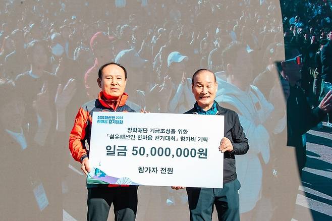 지난 26일 개최된 ‘2024 섬유패션인 한마음 걷기대회’에서 최병오 섬산련 회장이 한국패션봉제산업연합회 서울 지역 봉제업체 종사자 장학금 5000만원을 전달 받고 있다. [섬산련]