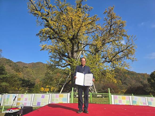 [당진=뉴시스] 지난 5일 경북 안동 용계리에서 열린 국가유산청 당산나무 할아버지 위촉식에서 김용성 이장이 위촉장을 받은 후 은행나무 앞에서 기념 촬영을 하고 있다. (사진=당진시 제공) 2024.11.06. photo@newsis.com *재판매 및 DB 금지