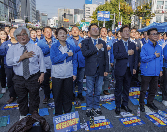 지난 11월2일 더불어민주당 이재명(앞줄 오른쪽 두번째) 당대표와 박찬대 원내대표를 비롯한 민주당 지도부와 의원들이 서울 중구 서울역 일대에서 더불어민주당 주도의 '김건희 윤석열 국정농단 규탄·특검 촉구 국민행동의 날' 집회에 참가해 국기에 경례하고 있다. 앞줄엔 김민석(오른쪽 첫번째) 민주당 최고위원과 그 친형이자 촛불승리전환행동(촛불행동) 상임대표인 김민웅 전 경희대 교수가 서 있다.<연합뉴스 사진 갈무리>