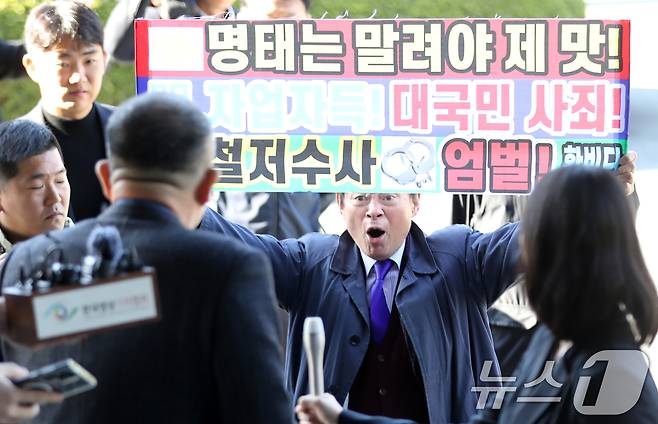 윤석열 대통령 부부 공천 개입 의혹의 핵심 인물인 명태균 씨가 9일 오전 정치자금법 위반 혐의 피의자 신분으로 검찰 조사를 받기 위해 경남 창원시 성산구 창원지방검찰청으로 출석하며 '명태는 말려야 제맛' 등이 적힌 현수막을 든 한 유튜버와 실랑이를 벌이고 있다. 청사로 들어가는 명 씨 뒤에서 한 유튜버가 "어제는 꼬리내리고＂라고 비난하자 명 씨는 뒤돌아서 ＂정신차려＂라고 호통쳤다. 2024.11.9/뉴스1 ⓒ News1 윤일지 기자