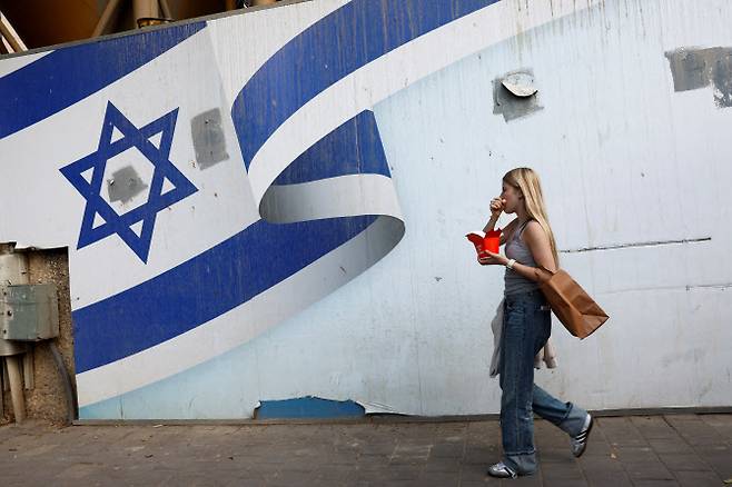 10일(현지시간) 이스라엘 텔아비브에서 이스라엘과 하마스 간 가자지구 분쟁이 계속되는 가운데 한 여성이 이스라엘 국기 벽화 앞을 지나가고 있다. (사진=로이터)