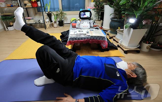 돌봄로봇 다솜K(다솜이)를 이용 중인 어르신이 18일 오후 서울 금천구 자택에서 돌봄로봇에게 추천 받은 허리 운동 동영상을 보며 동작을 따라하고 있다. 나홀로 가구인 이 어르신은 돌봄로봇 다솜이와의 소통을 통해 요리, 운동 등 다양한 기능을 비롯해 외로울 때 말벗이 되어 주는 점에서 매우 만족한다고 밝혔다. 2024.11.18/뉴스1 ⓒ News1 박정호 기자