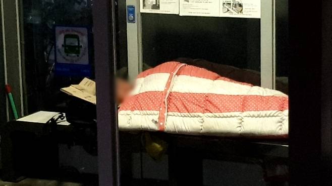 방풍 시설이 설치된 서귀포시의 한 버스정류장 온열 의자 위에서 이불을 덮고 잠을 자는 한 남성 (사진, 제주자치도에 바란다)