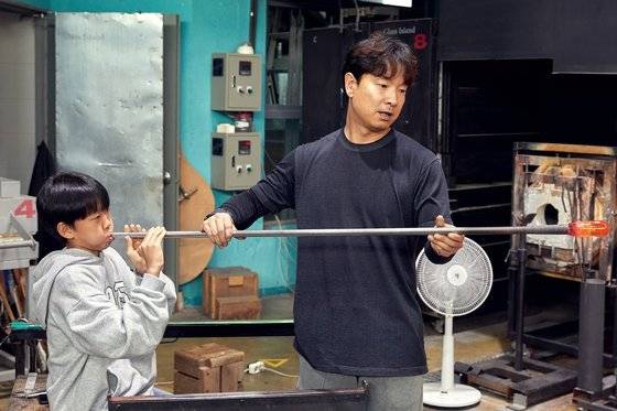 유영조(오른쪽) 작가가 소중 학생기자단에게 유리를 파이프로 말아내어 대롱불기를 한 뒤 여러 도구를 사용해 형태를 가공하는 블로잉 기법에 대해 알려주고 있다.