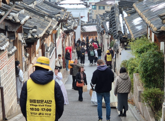 지난 1일 서울 종로구 북촌한옥마을 일대 관광객들 사이 계도요원이 서있다. 마을 방문 시간이 적힌 노란 조끼를 입은 이들은 관광객 출입을 통제하고 소음을 관리한다. 지난달 1일부터 북촌 일대에서는 오후 5시부터 다음 날 오전 10시까지 외부인 출입을 제한하는 레드존 제도가 시행되고 있다. 2024.12.1 김우진 기자