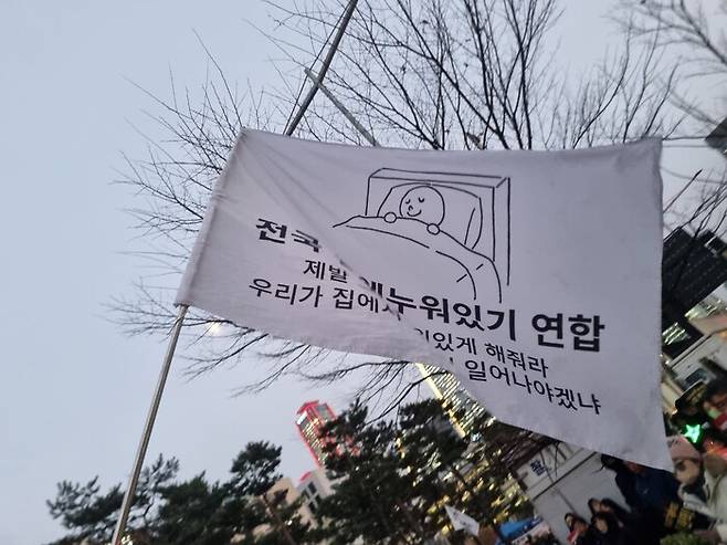 12일 저녁 6시 서울 영등포구 국회의사당역 5번 출구 앞에서 열린 ‘내란수괴 윤석열 즉각 탄핵! 시민촛불’ 집회에 ‘전국 집에 누워있기 연합’ 깃발이 휘날리고 있다. 고나린 기자