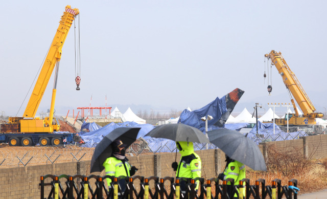 ▲5일 오전 우산을 쓰고 근무하는 경찰관들 뒤로 전남 무안국제공항 사고현장 및 꼬리 날개에 방수포가 덮여 있다. 2025.1.5ⓒ연합뉴스