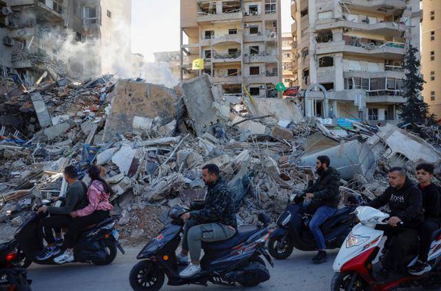 레바논 수도 베이루트 남부에 위치한 타유네 지역에서 지난해 11월 이스라엘군 폭격에 맞아 무너진 건물 앞으로 주민들이 스쿠터를 타고 지나가고 있다. 베이루트=로이터 연합뉴스