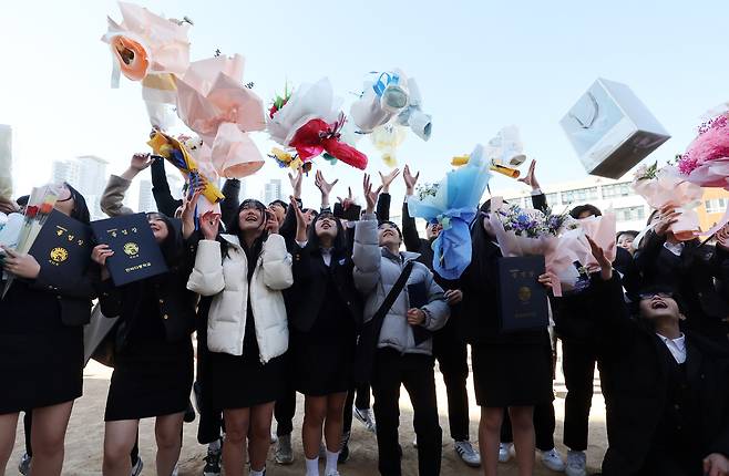 졸업생들이 운동장에서 꽃다발을 던지며 졸업을 축하하고 있다. 송봉근 기자