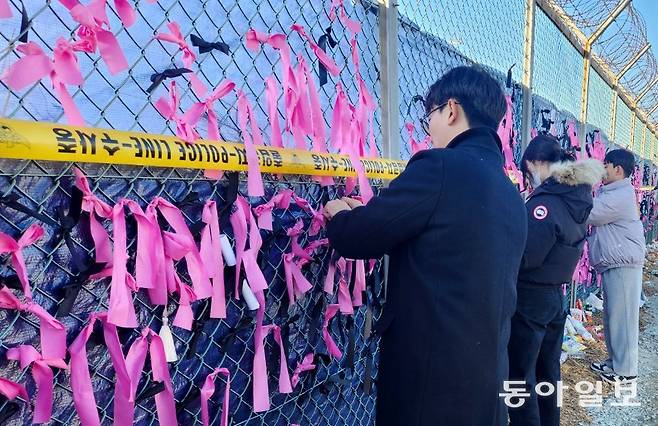 17일 오후 무안 제주항공 참사 현장을 방문한 희생자 유가족과 대학생 자원봉사자들이 현장 인근에 있는 철제 울타리에 분홍색 리본 1229개를 묶고 있다. 정부는 18일 오전 무안국제공항청사 2층에서 합동추모식을 열 예정이다. 무안=이형주 기자 peneye09@donga.com