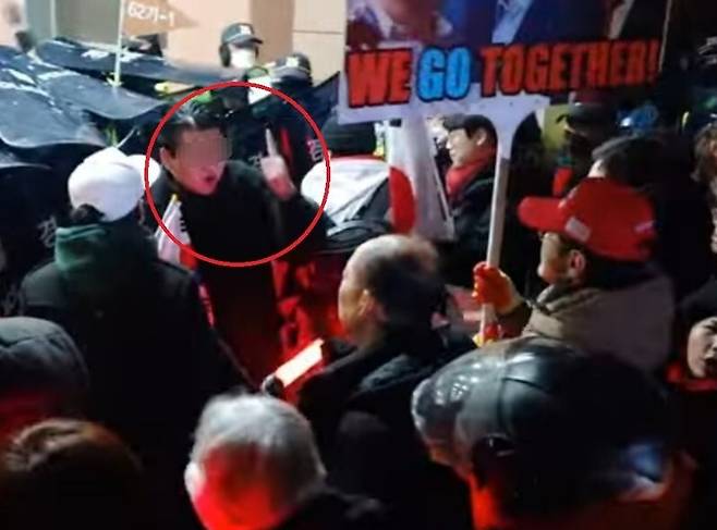 19일 새벽 서울서부지법 청사 밖에서 ‘내란 우두머리 피의자’ 윤석열 대통령 지지자들과 경찰이 대치하는 가운데, 한 참석자가 선두에 서 수신호를 하고 있다. 유튜브 채널 락티브이(TV) 갈무리