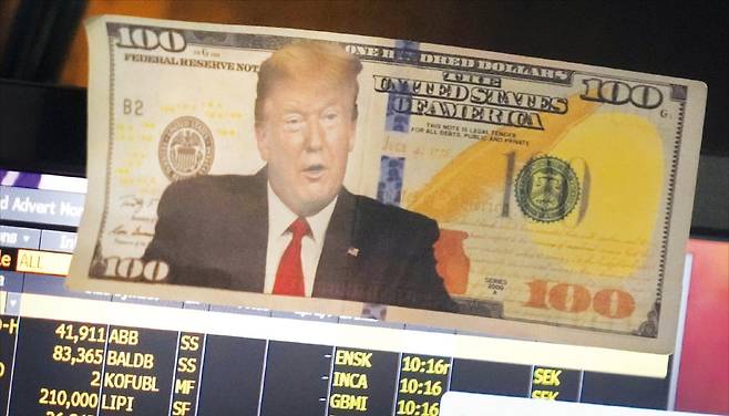 < ‘美 건국의 아버지’ 100달러에 프린트된 트럼프 > 21일(현지시간) 미국 뉴욕증권거래소 모니터 화면에 도널드 트럼프 대통령의 모습이 담긴 가짜 100달러 지폐가 붙어 있다. 원래 100달러 지폐 인물은 미국 ‘건국의 아버지’ 중 한 명인 벤저민 프랭클린이다. /AP연합뉴스